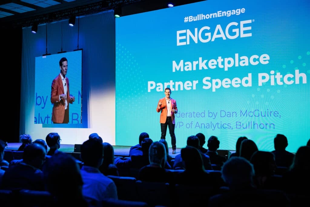 A presenter stands on stage at the Engage conference, addressing an attentive audience