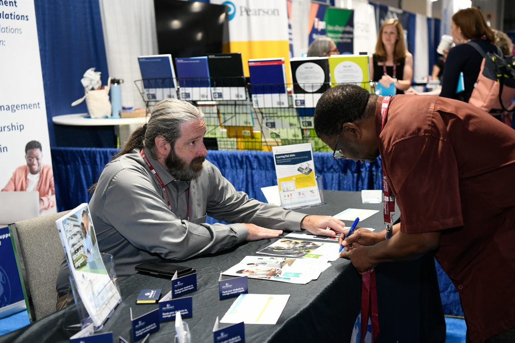 Two attendees speaking at an exhibitor booth during the AOM Annual Meeting