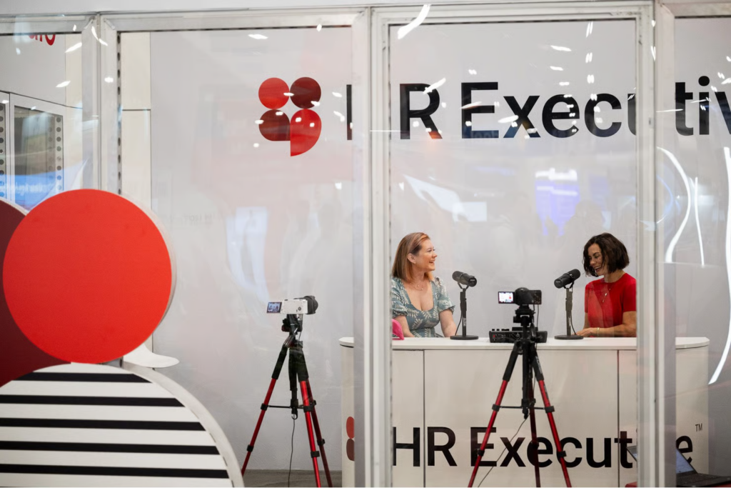 Due donne registrano un podcast presso uno stand marchiato HR Executive con microfoni e videocamere.