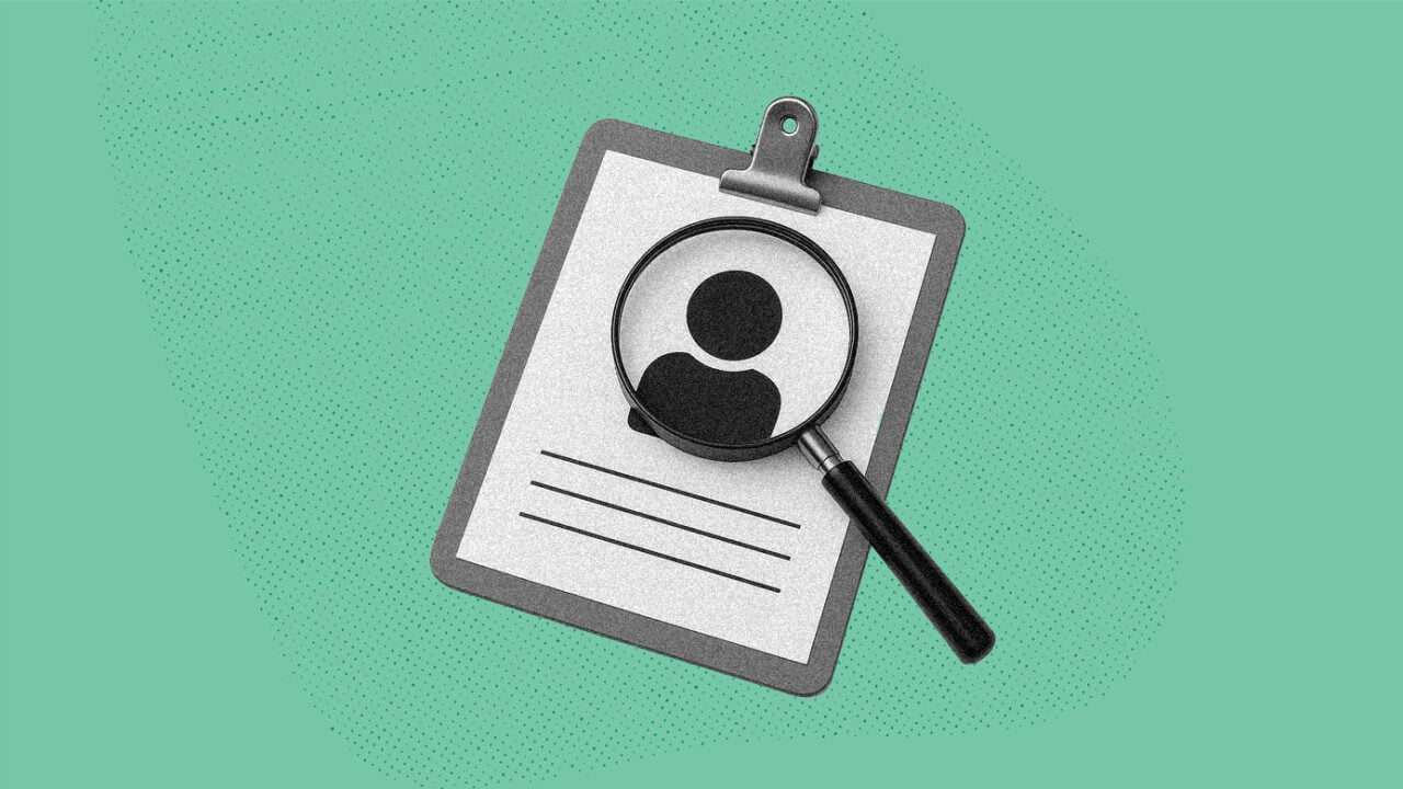 A magnifying glass hovers over a resume with a person icon on it to imply examining someone closely.